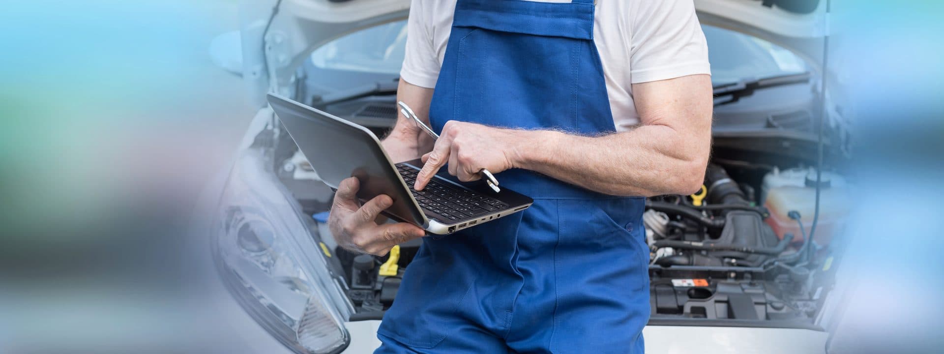 Mécanicien en salopette utilisant un logiciel de gestion sur ordinateur portable devant un moteur