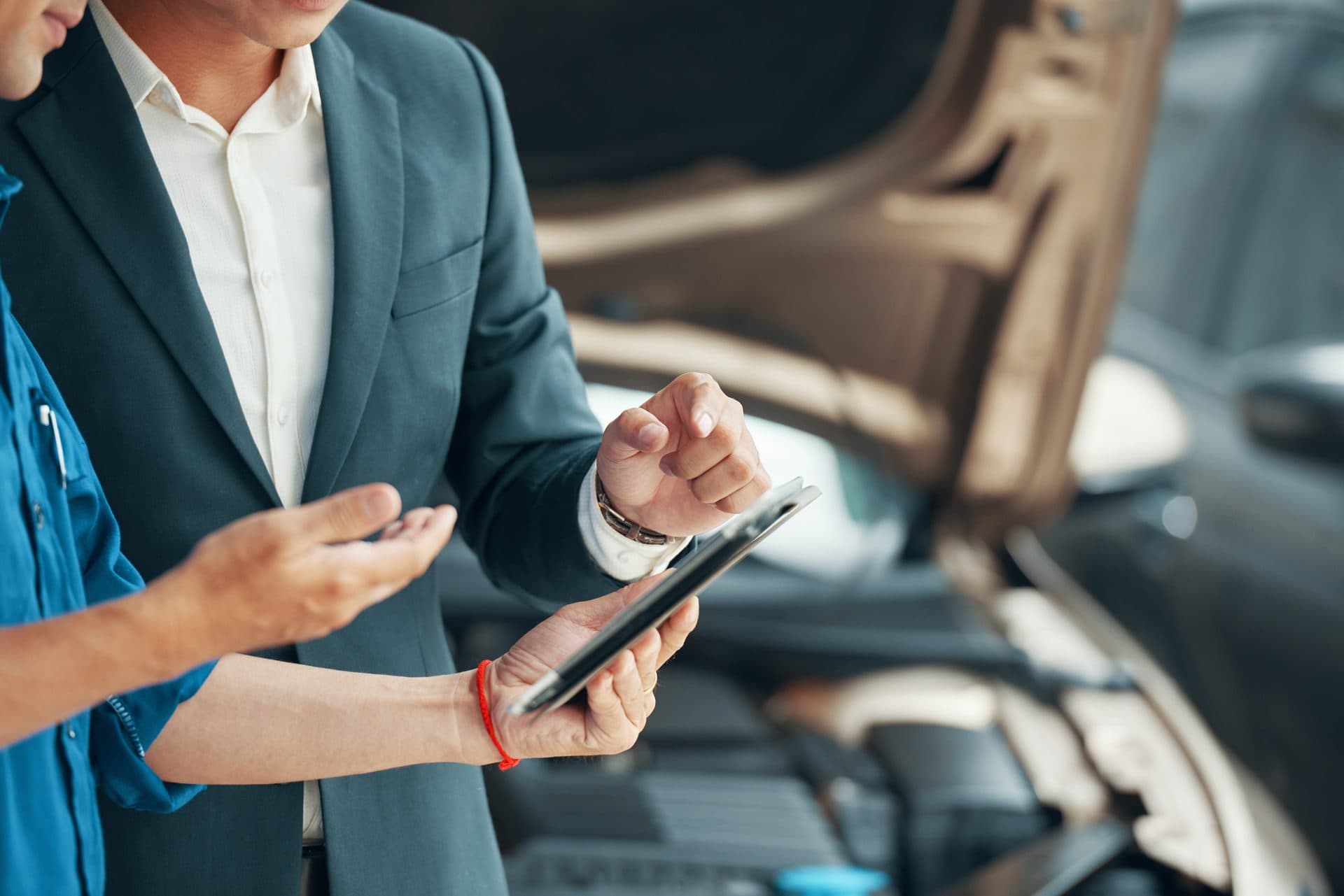 Conseiller de garage présentant un devis sur tablette à un client devant le capot ouvert