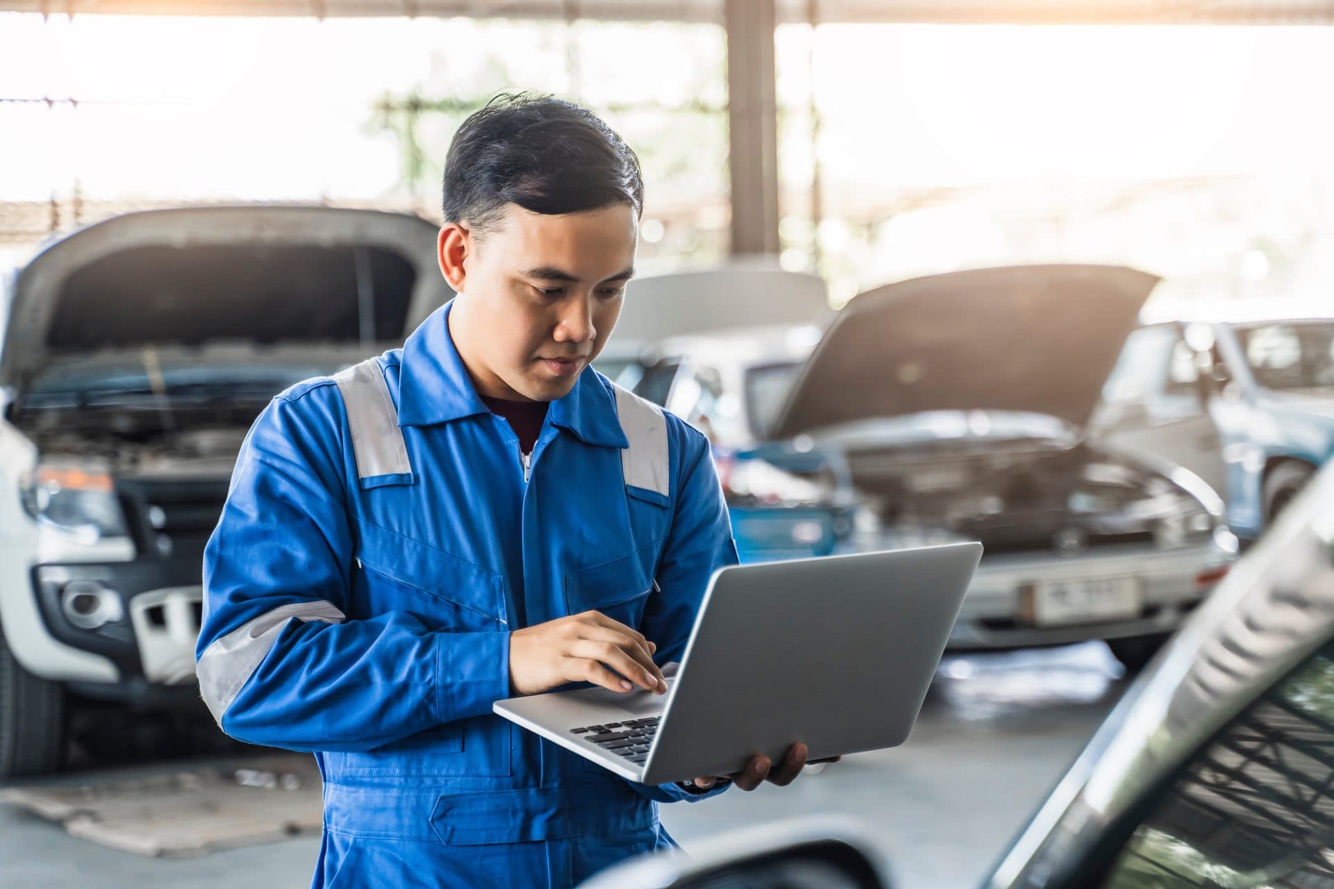 Mécanicien utilisant un logiciel de garage en ligne sur ordinateur portable au milieu de l'atelier